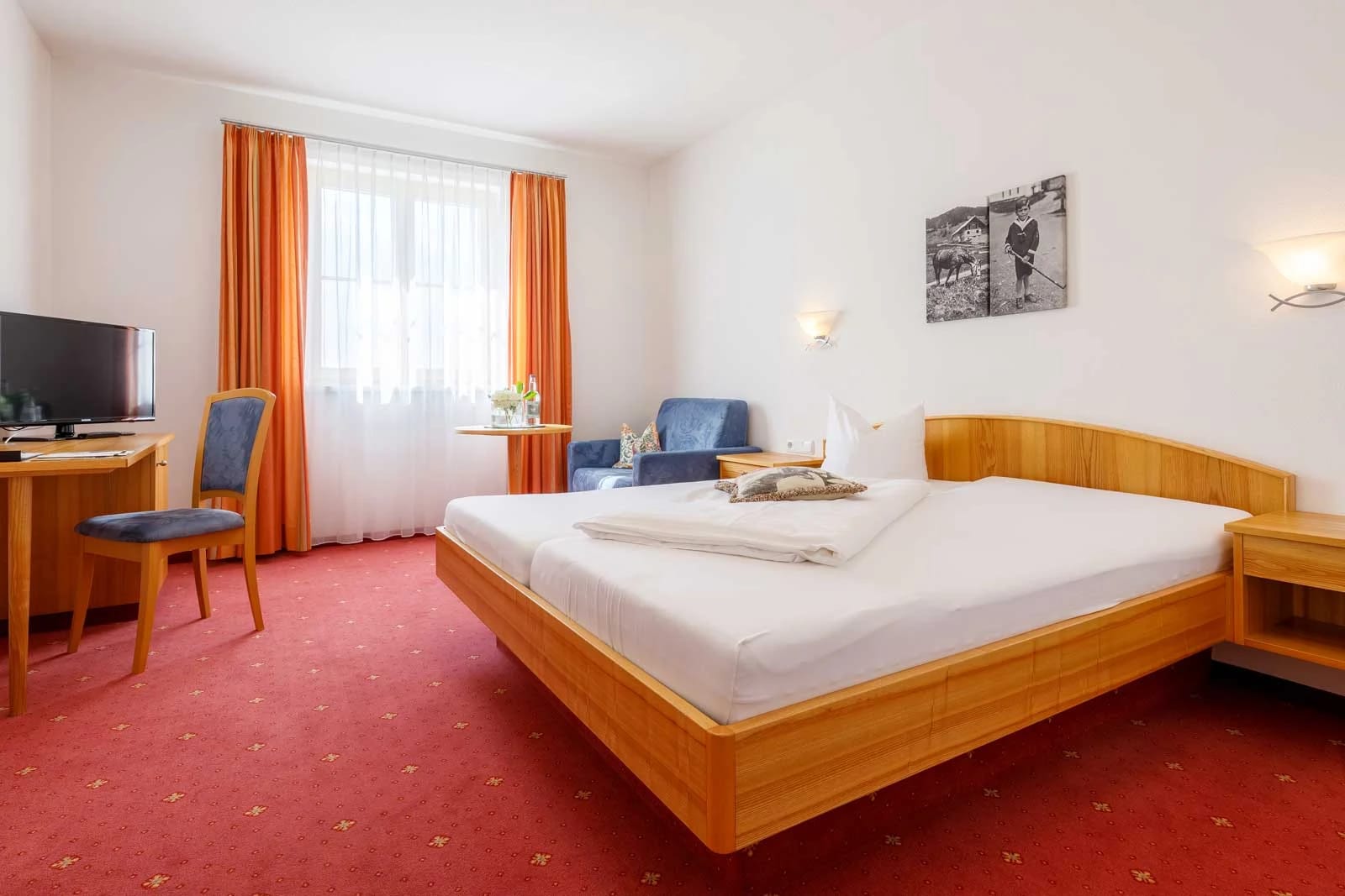 Geräumiges Doppelzimmer mit Holzbett, Sitzecke und Schreibtisch in warmen Farben
