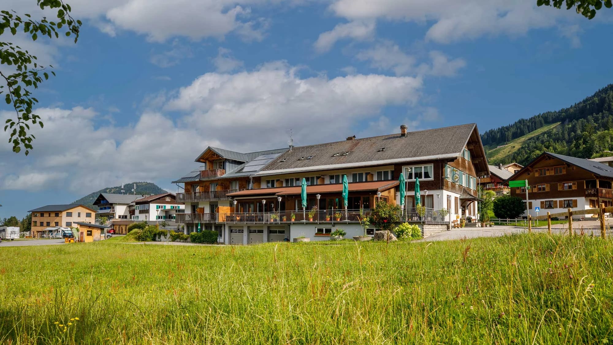 Das Hotel Der Hirschen im Dorf Sibratsgfäll, von der Wiese aus gesehen, eingebettet in die Bregenzerwälder Berglandschaft