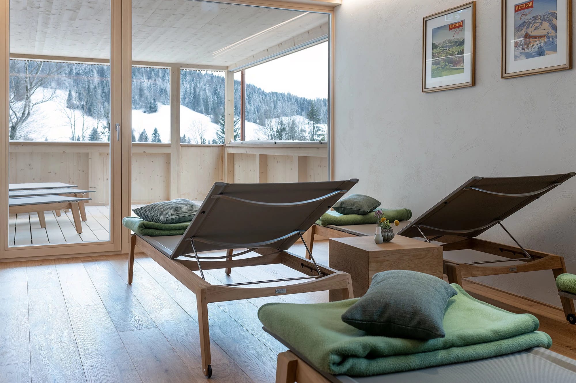 Ruheraum mit Liegen und grünen Decken vor einer Fensterfront mit Blick auf die verschneite Landschaft