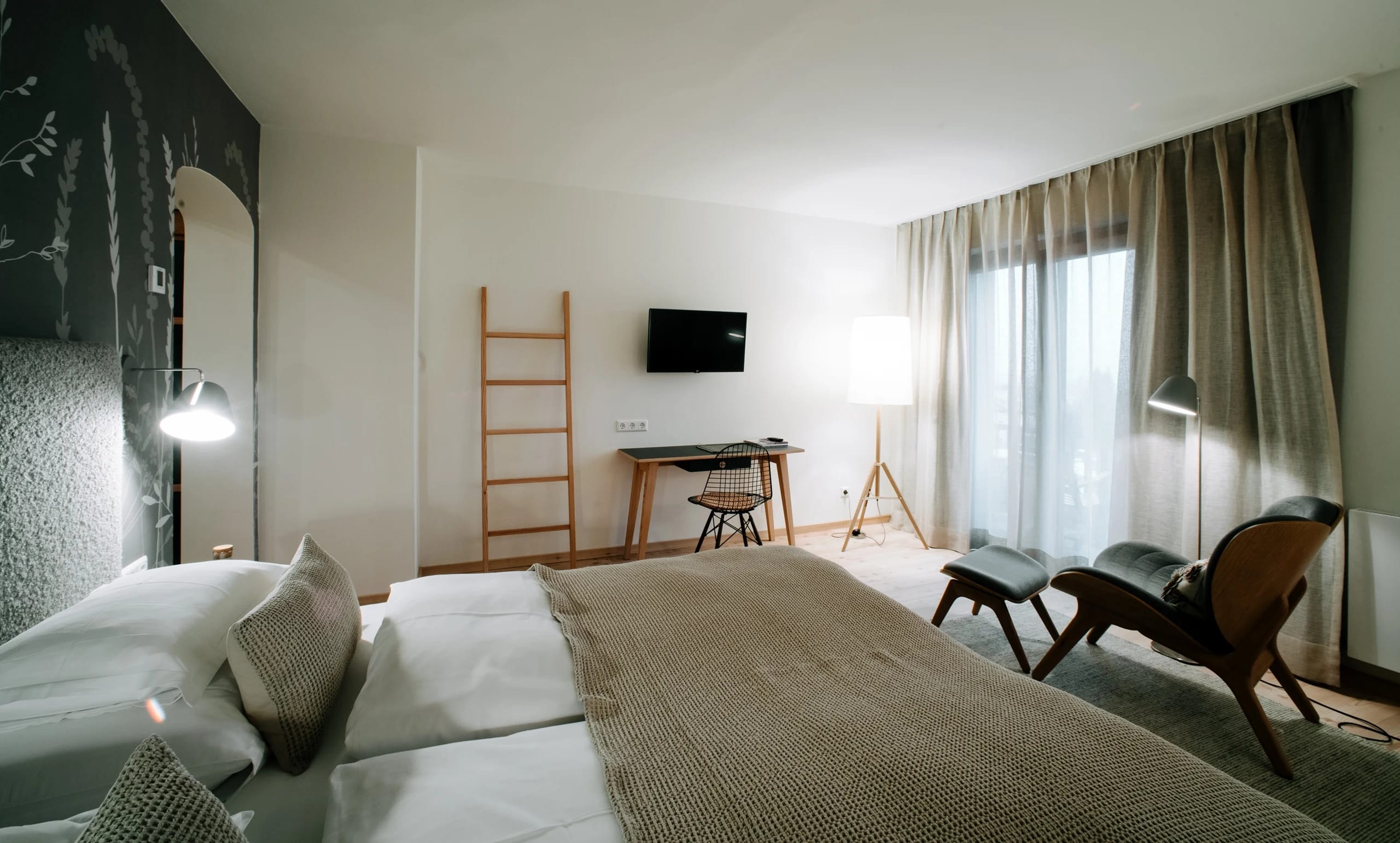 Hotelzimmer mit Doppelbett, Sessel, Schreibtisch und großem Fenster