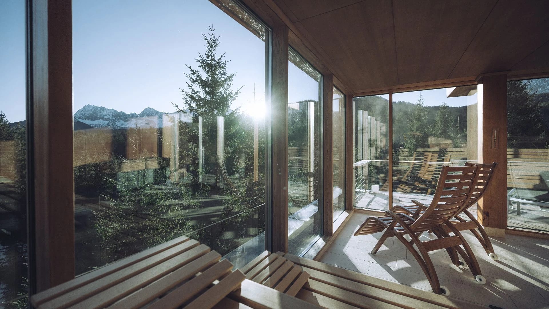 Saunakabine mit Holzbänken und Panoramafenstern, davor Holzliegen auf der Terrasse