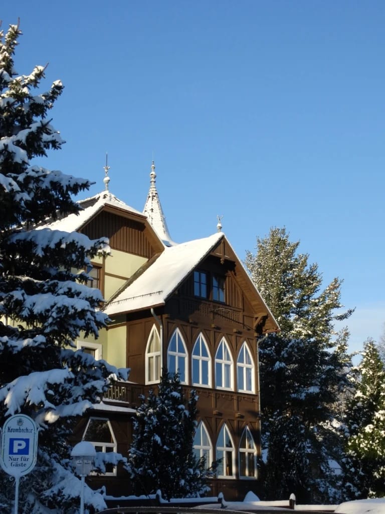 Holzfassade mit Spitzbogenfenstern und Türmchen im Schnee bei blauem Himmel