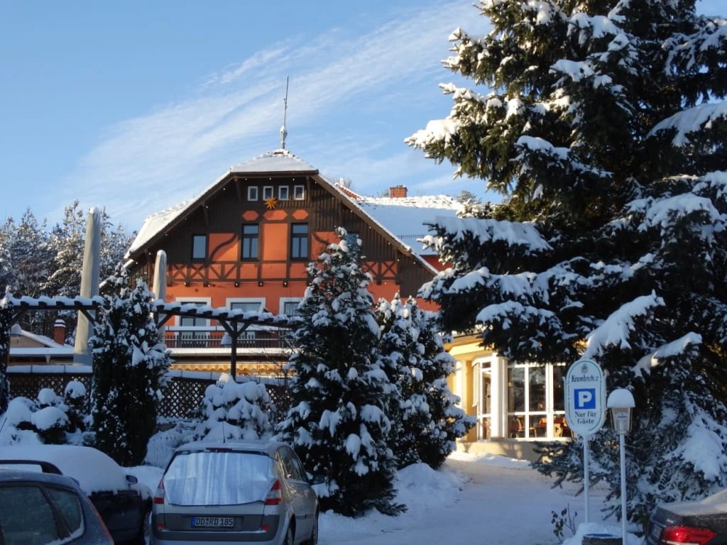 Rot-weißes Fachwerkhaus im Schnee hinter verschneiten Tannen bei blauem Himmel