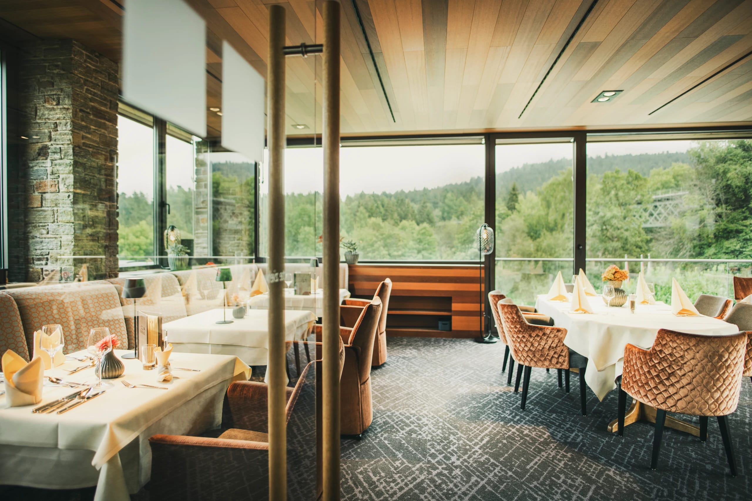 Restaurant mit eingedeckten Tischen, Korbstühlen und Panoramafenstern mit Blick ins Grüne