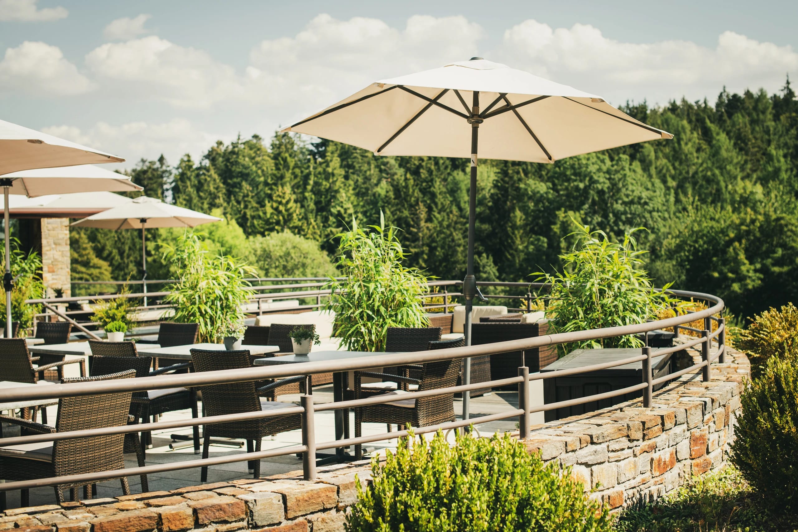 Terrasse mit Holztischen, Korbstühlen und Sonnenschirmen mit Blick auf den Wald