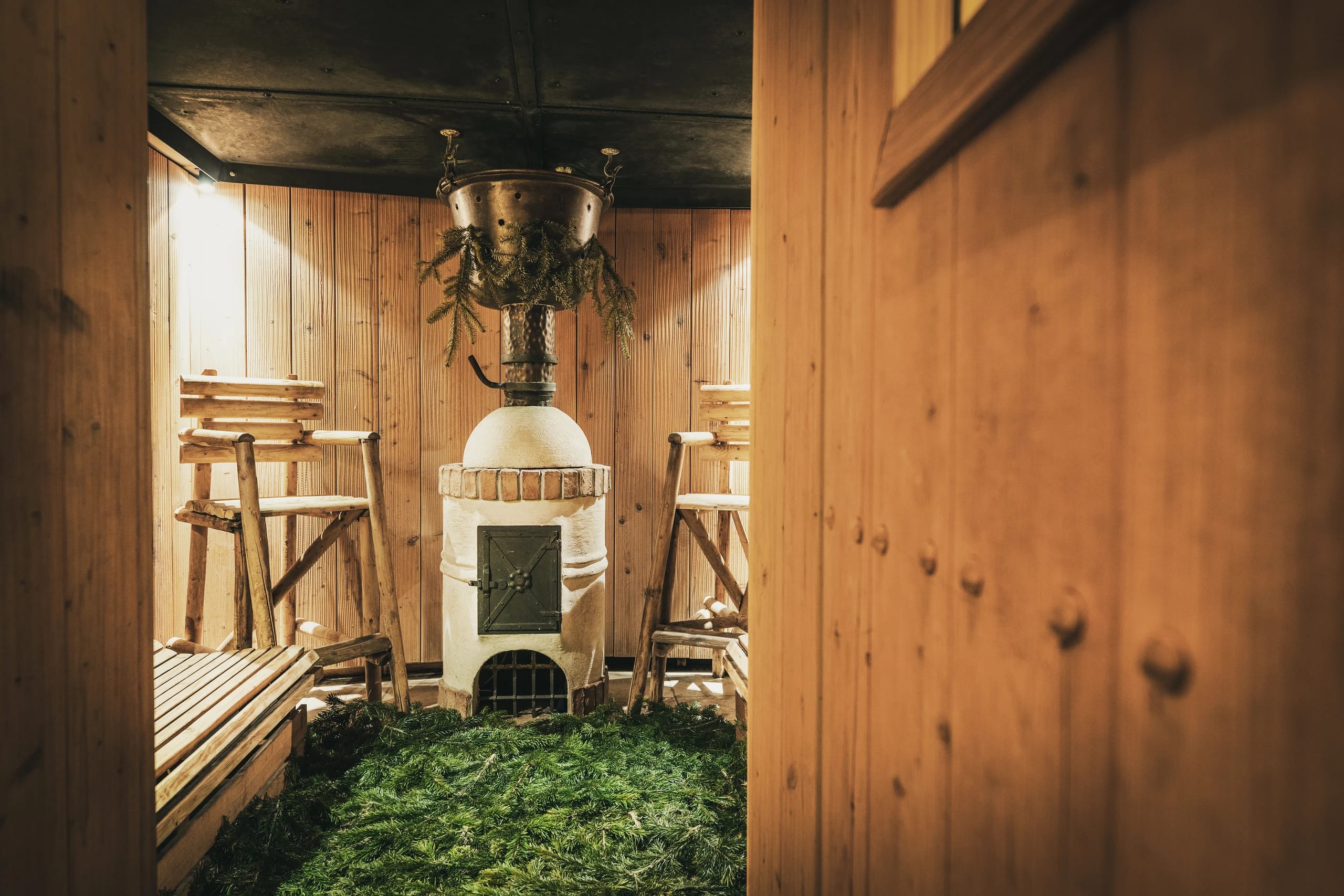Blick in die Holzsauna mit Saunaofen und frischen Tannenzweigen auf dem Boden
