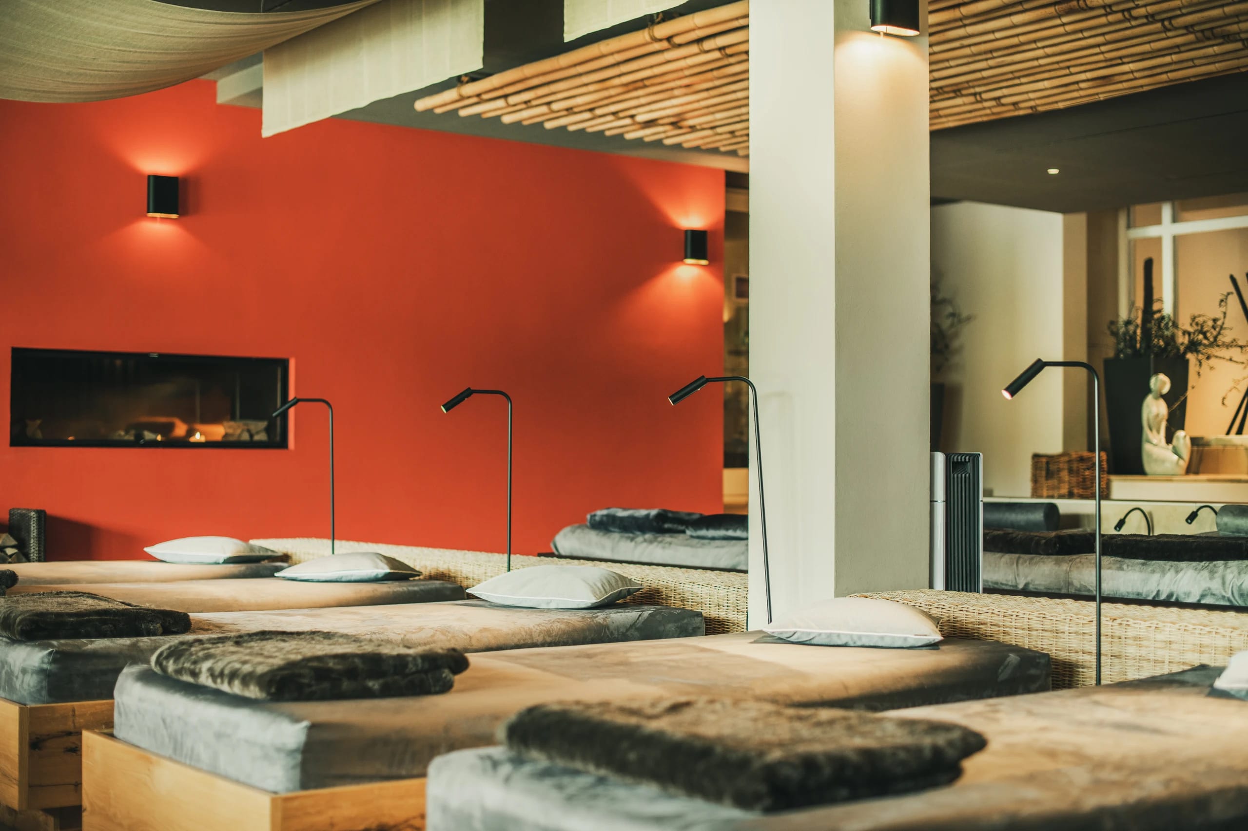 Ruheraum mit roter Wand, Kamin und gepolsterten Liegen unter einer Holzlattendecke