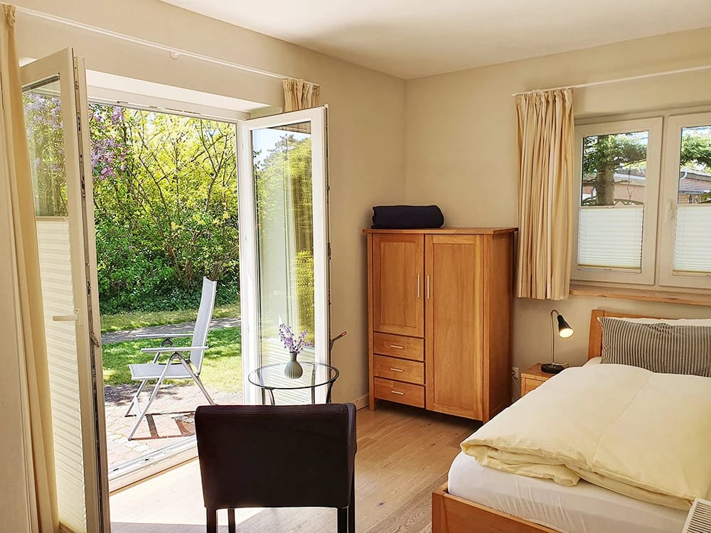 Zimmer mit Bett, Kleiderschrank und geöffneter Terrassentür zum begrünten Garten