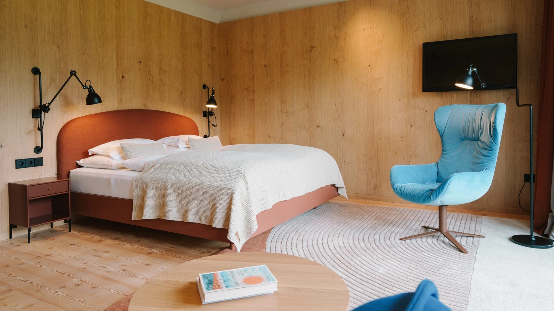 Mit hellem Holz ausgekleidetes Hotelzimmer mit Doppelbett und Sessel