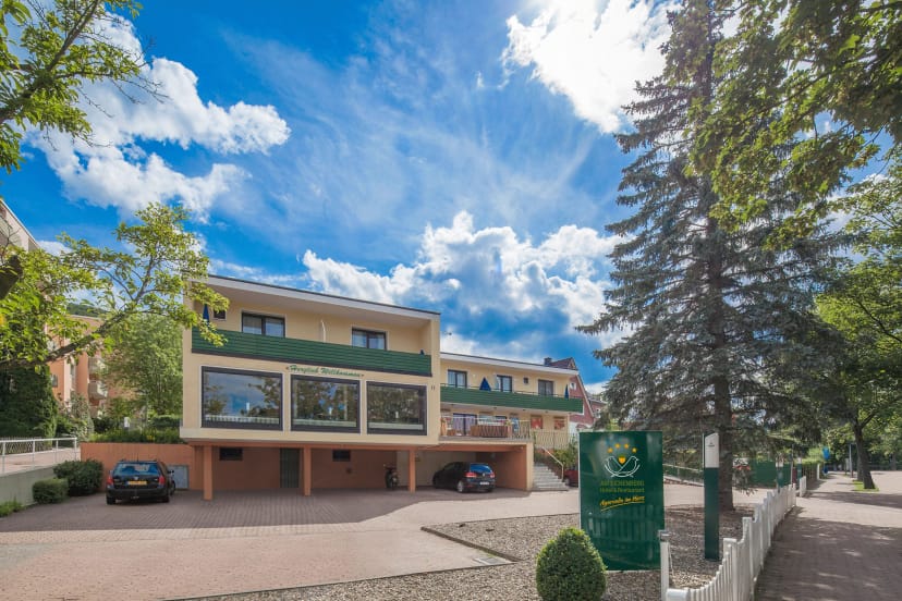 Außenansicht des Hotelgebäudes mit Vorfahrt, geparkten Autos und hohen Nadelbäumen