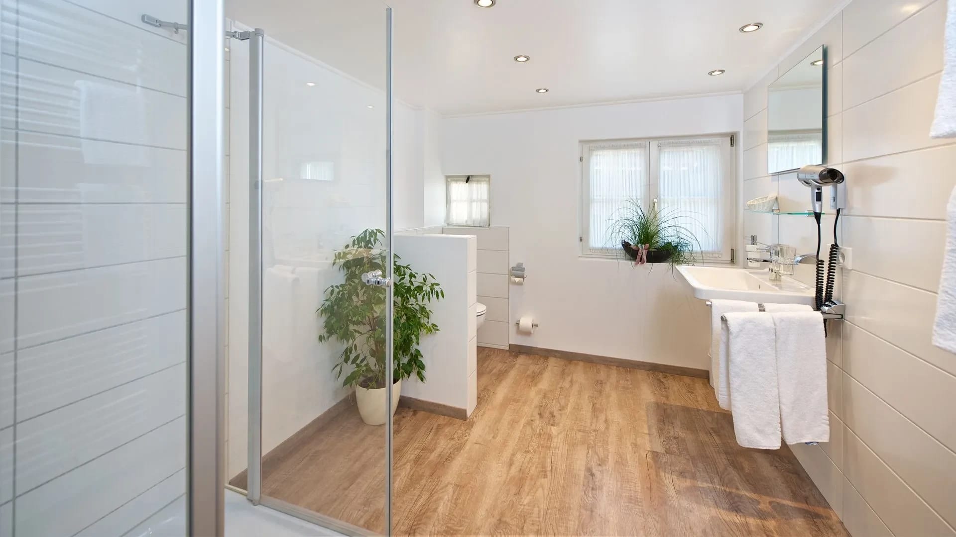 Modernes Badezimmer mit begehbarer Glasdusche, Waschbecken mit Handtüchern, Fenster und Boden in Holzoptik
