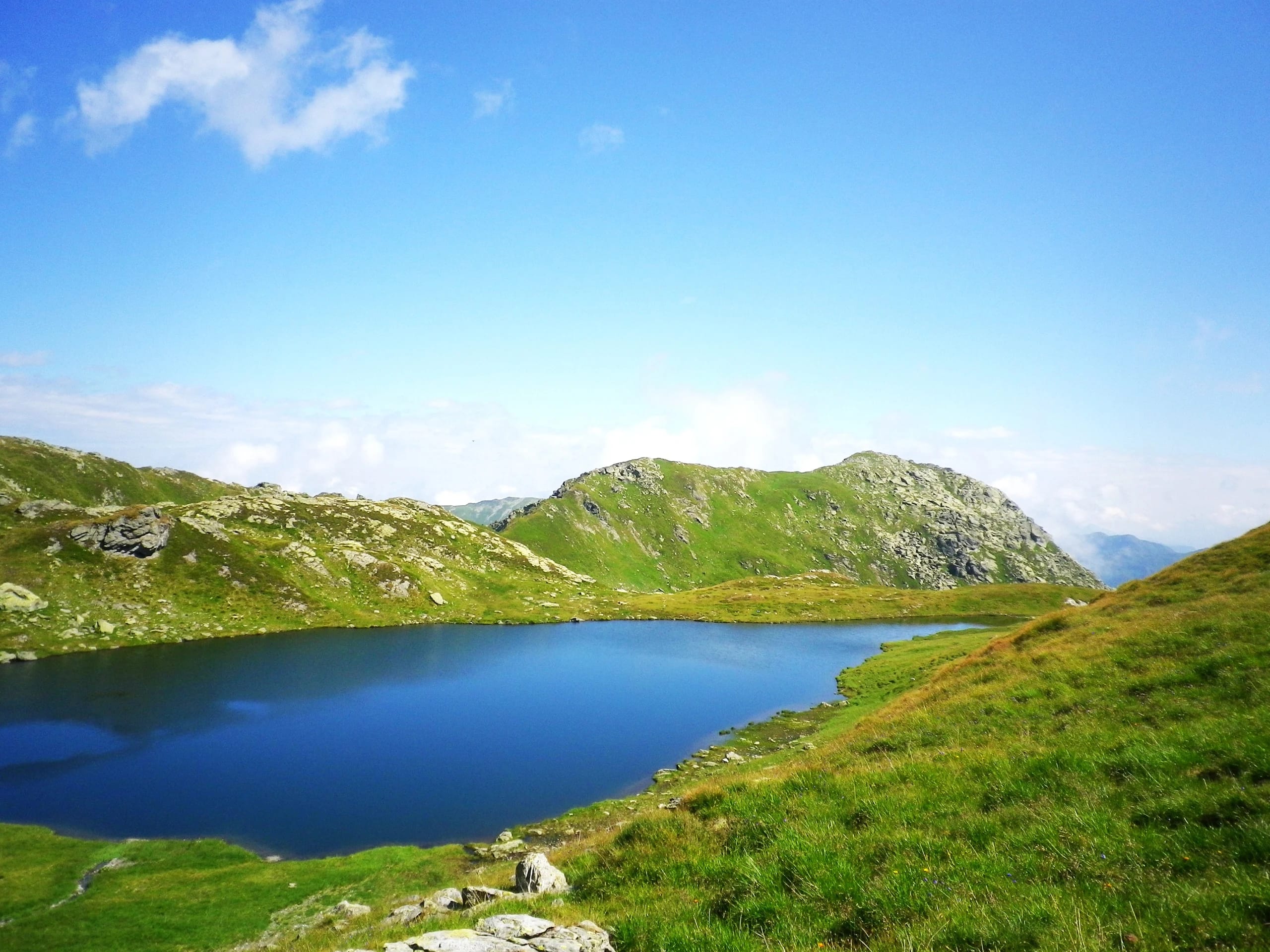 Bergsee mit grünen Hängen und Felsrücken unter blauem Himmel