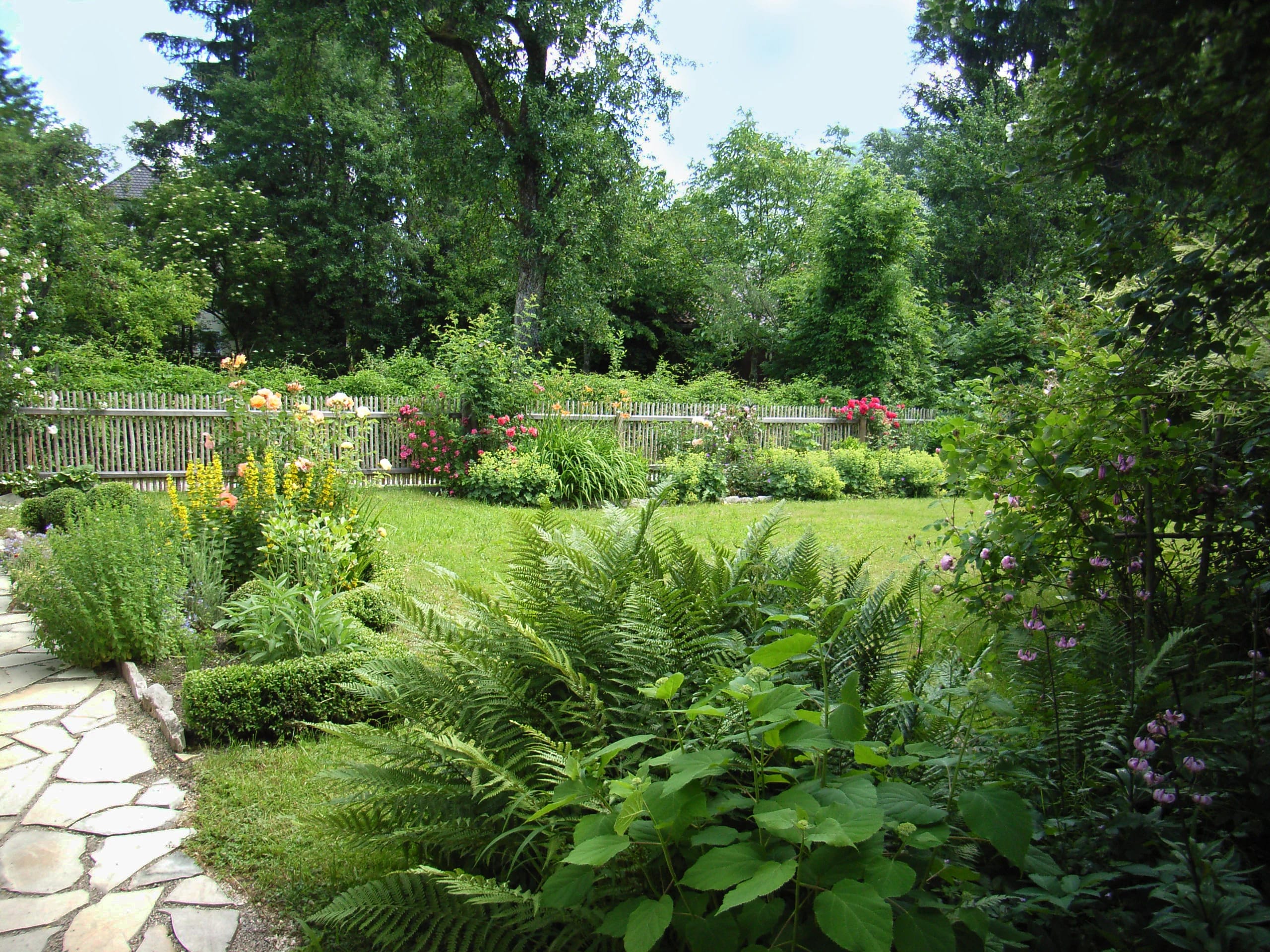 Garten mit Rasenfläche, Staudenbeeten, Holzzaun und Natursteinweg