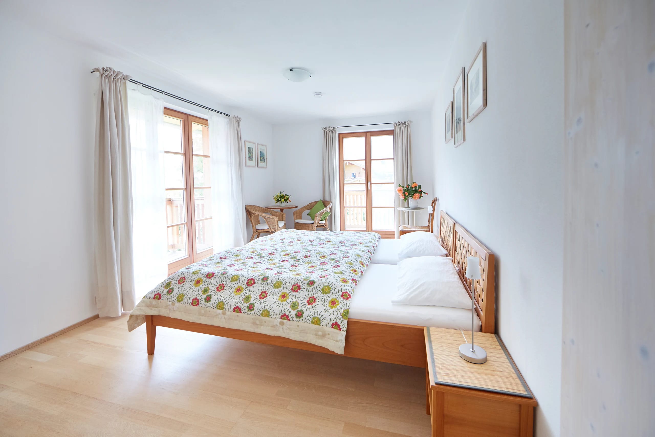 Helles Doppelzimmer mit Holzboden, geblümter Bettdecke und zwei Fenstertüren
