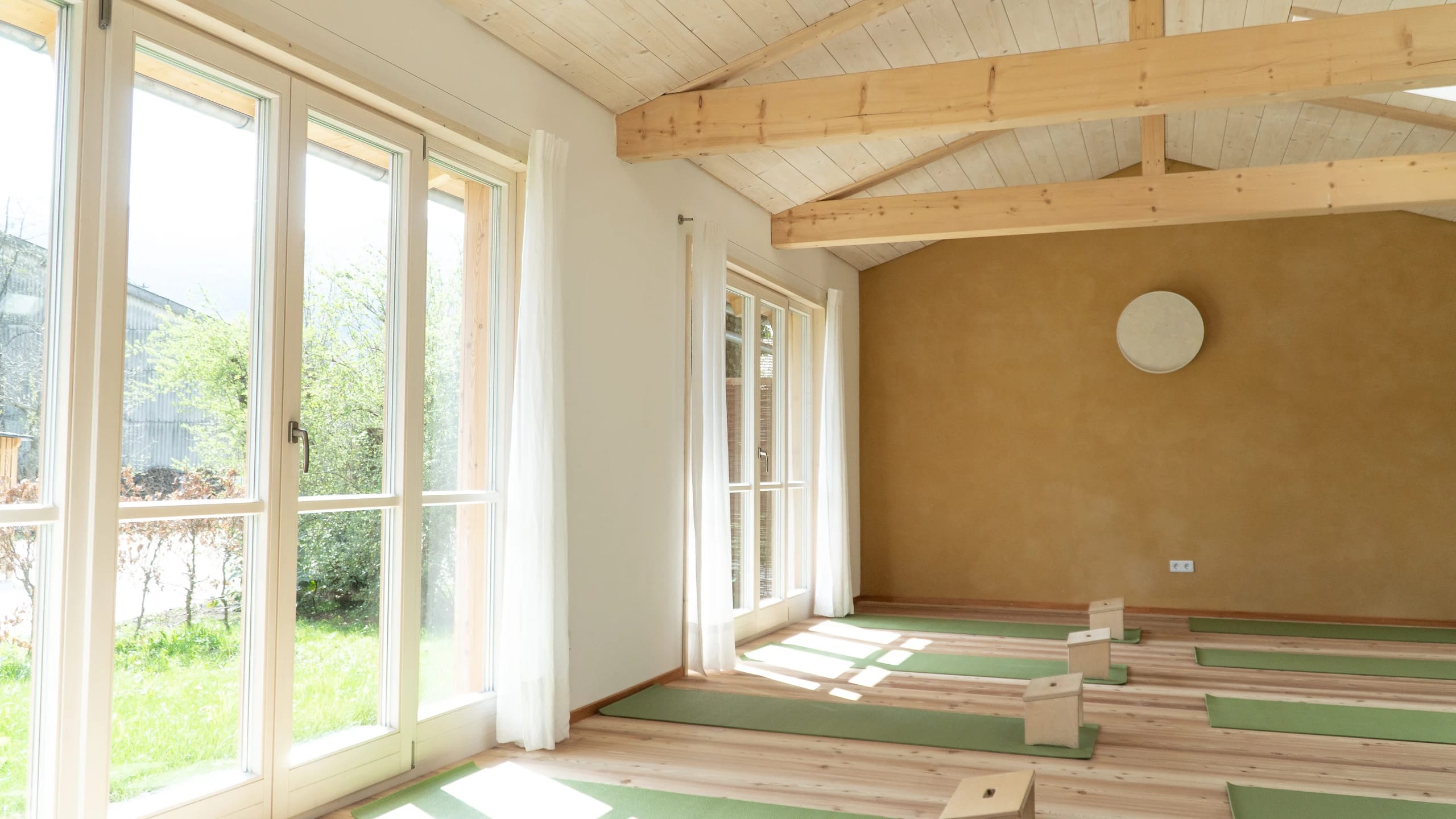 Gymnastikraum mit Holzdecke, bodentiefen Fenstern zum Garten und ausgelegten Matten