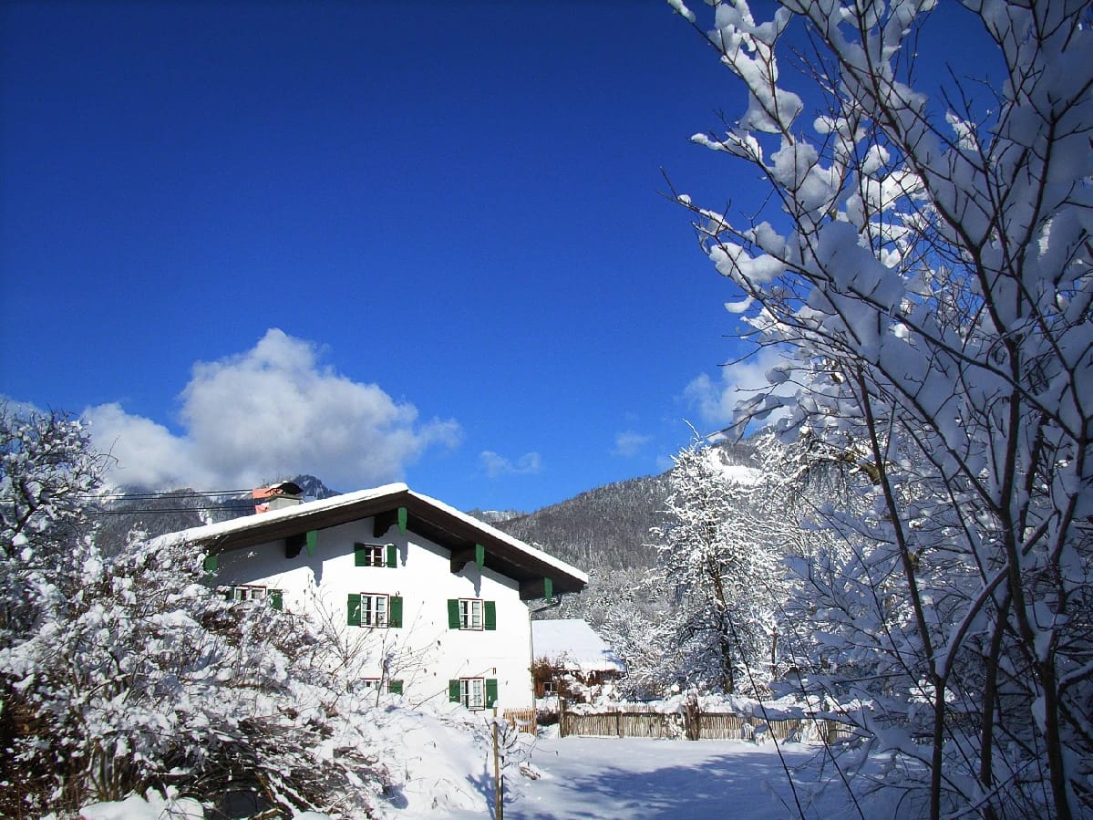Das Haus im Schnee vor blauem Himmel, dahinter verschneite Berge