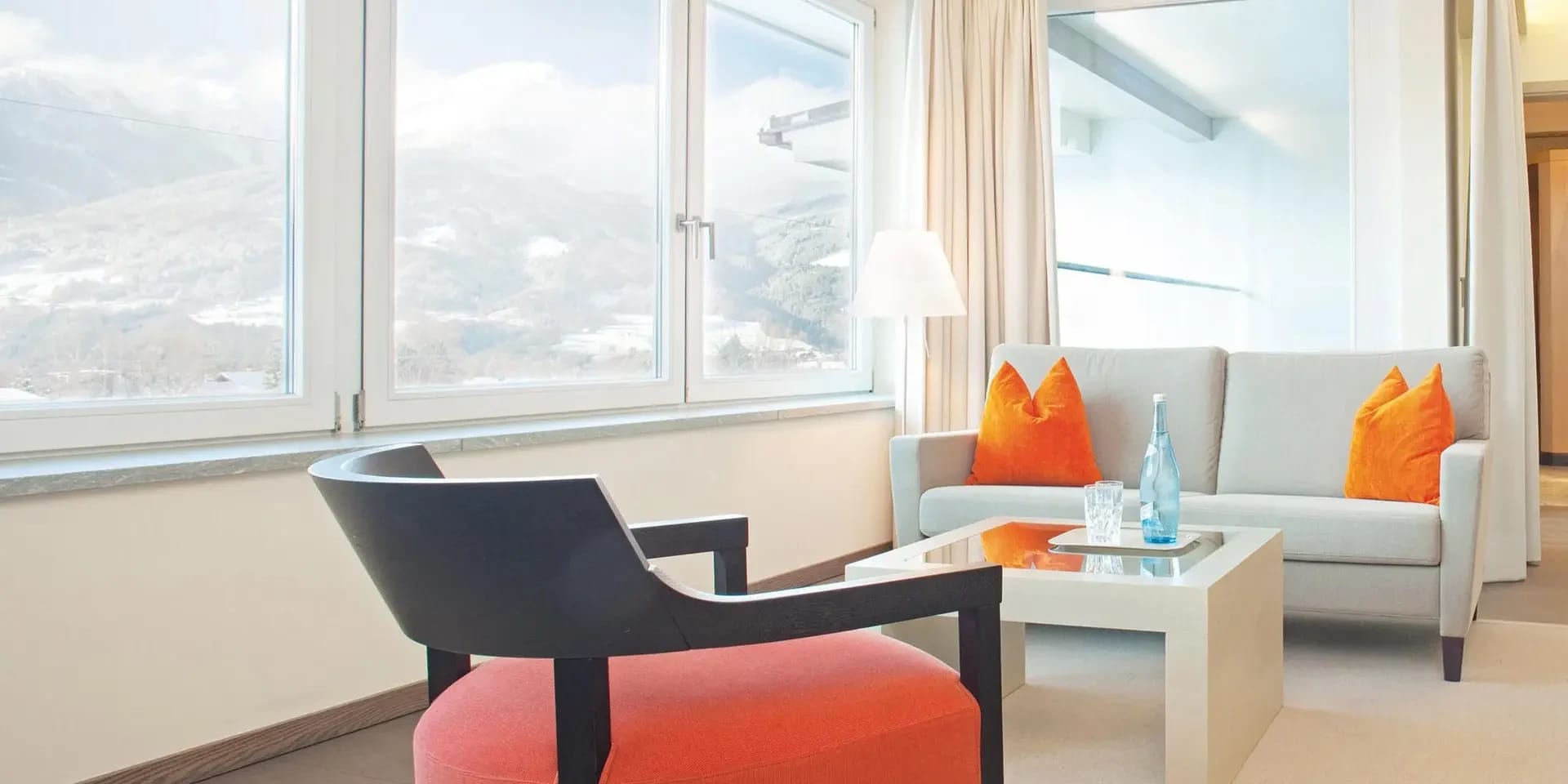 Sitzecke im Zimmer mit Sessel, Sofa und Eckfenstern mit Blick auf verschneite Berge
