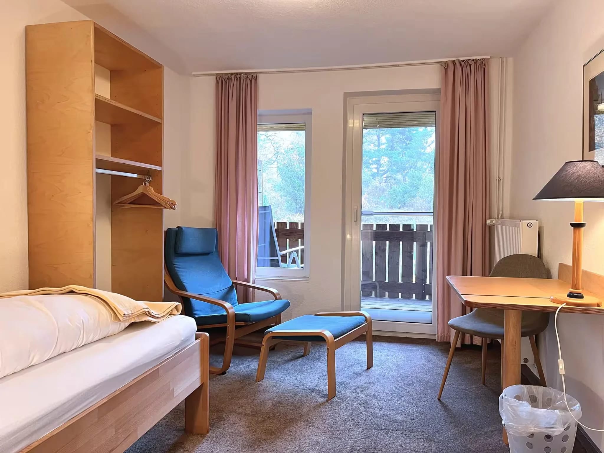 Einzelzimmer mit Sessel und Fußhocker, Schreibtisch und Balkontür