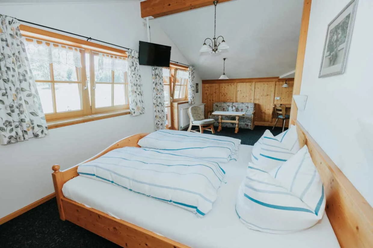Zimmer mit Doppelbett aus hellem Holz, Sitzecke am Fenster und Dachschräge