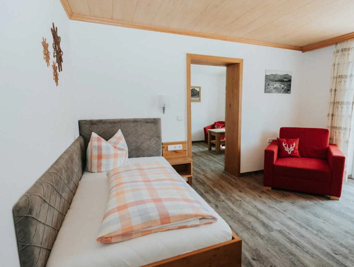Einzelzimmer mit Bett, rotem Sessel und Durchgang zum Nebenzimmer