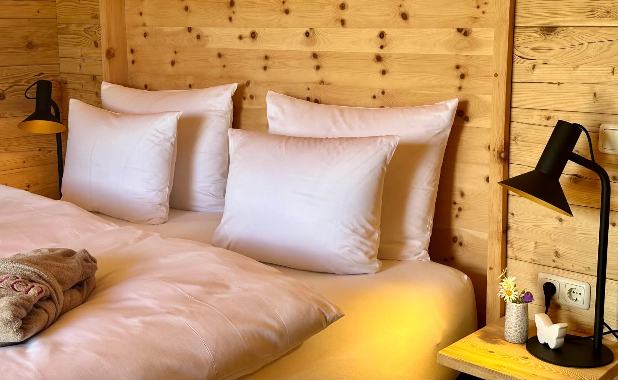 Doppelbett mit weißer Bettwäsche vor holzvertäfelter Wand