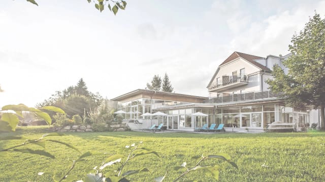 Außenansicht des Gesundheitshotels Klosterberg mit Glasfront, Sonnenterrasse und Gartenwiese im Sommer