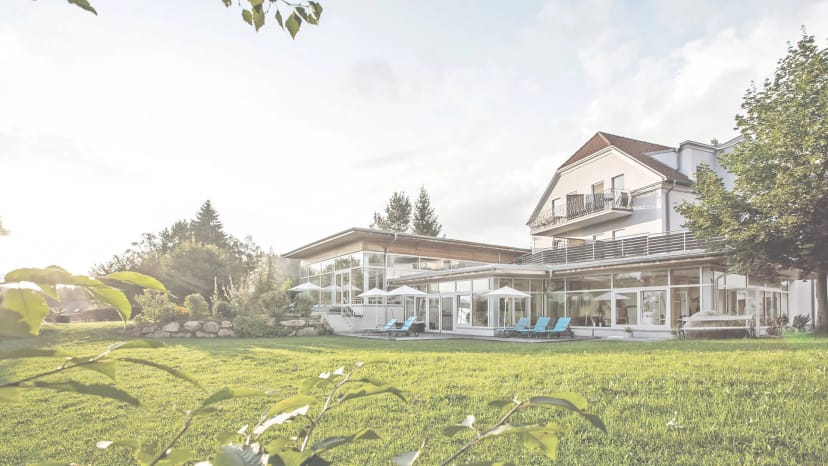Außenansicht des Gesundheitshotels Klosterberg mit Glasfront, Sonnenterrasse und Gartenwiese im Sommer