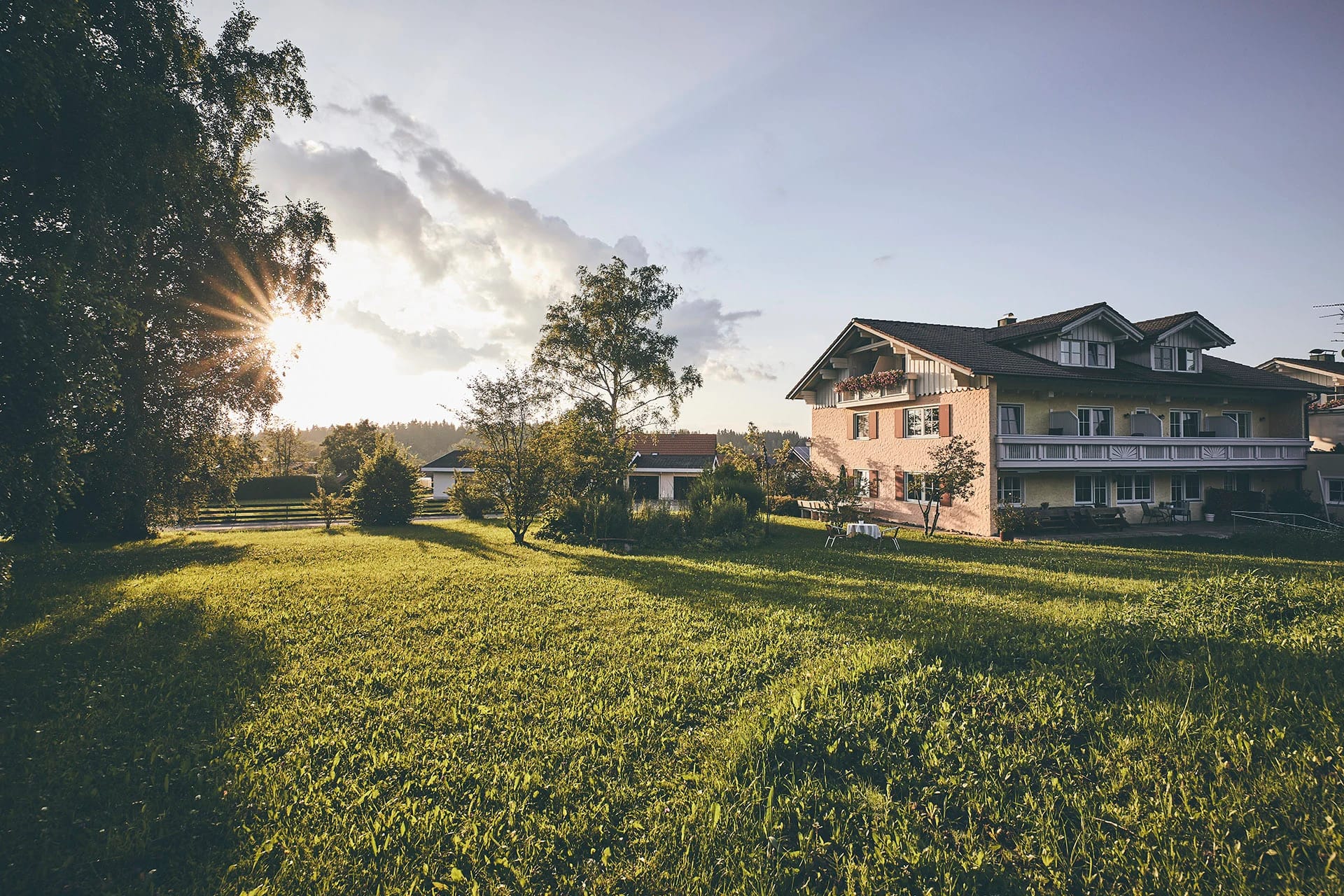 Hotelgebäude mit Balkonen im Abendlicht, davor eine große Wiese mit Bäumen