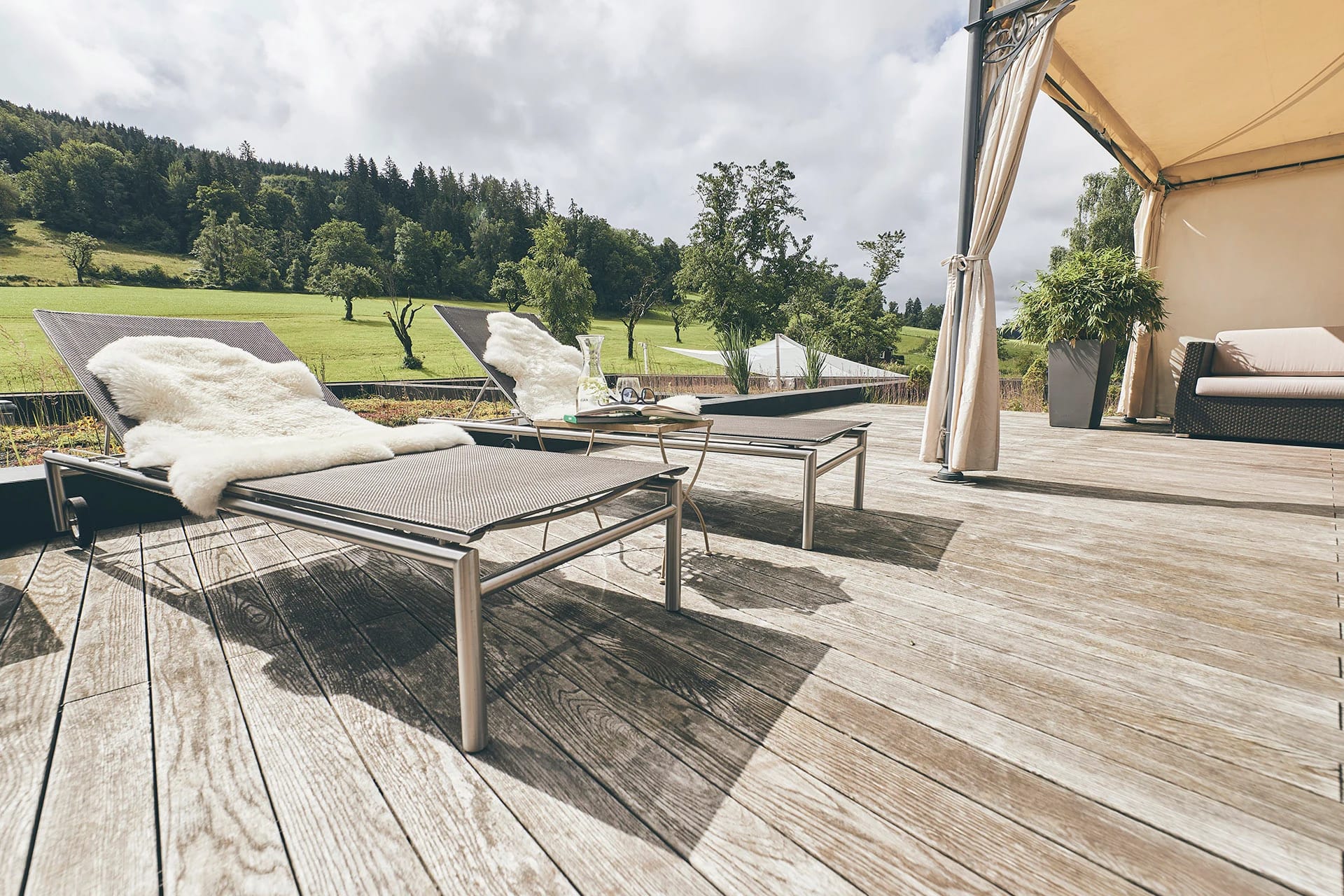 Sonnenterrasse aus Holz mit Liegen und Blick über Wiesen auf bewaldete Hügel