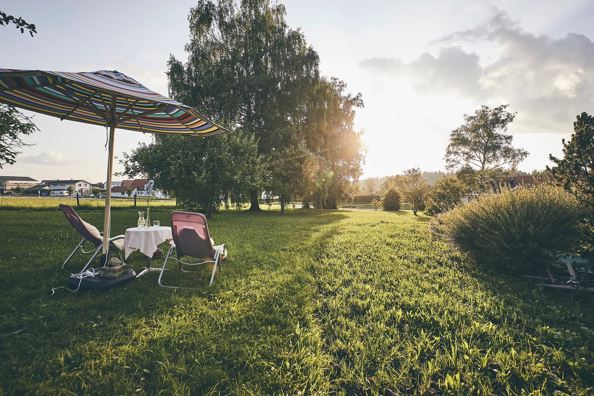 Liegewiese mit Sonnenschirm, Liegestühlen und Tisch im Abendlicht