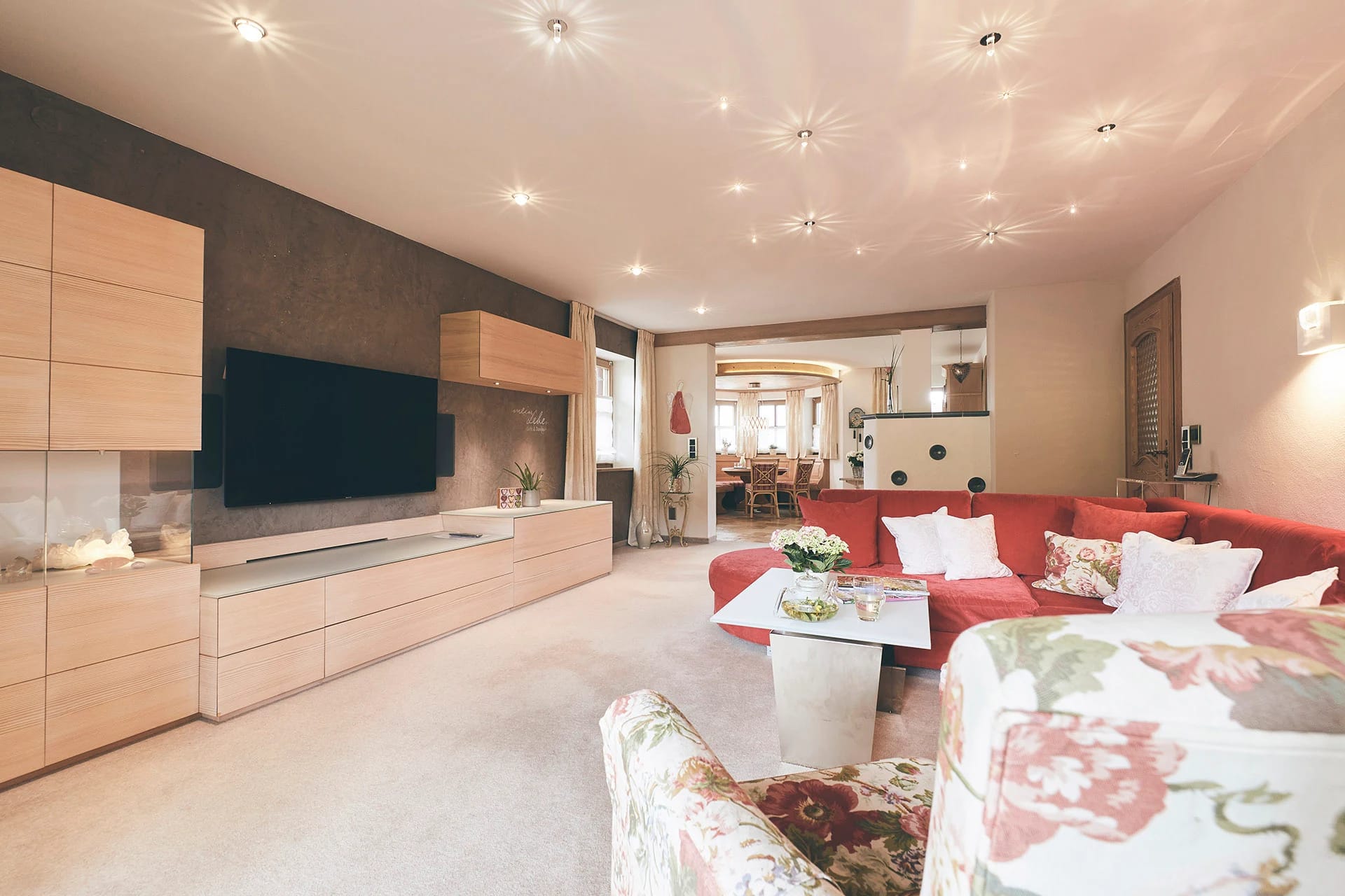 Wohnraum mit roter Couch, gemusterten Sesseln und Fernseher