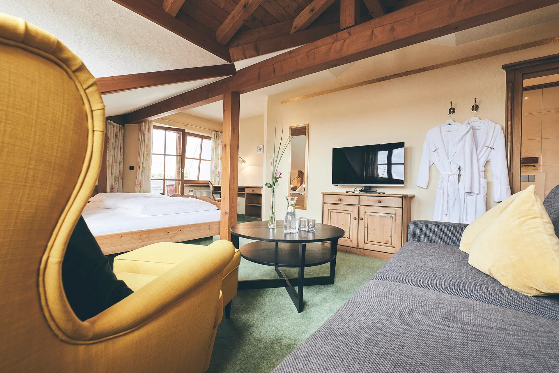 Dachzimmer mit Holzbalken, Doppelbett, Sitzecke und Fernseher