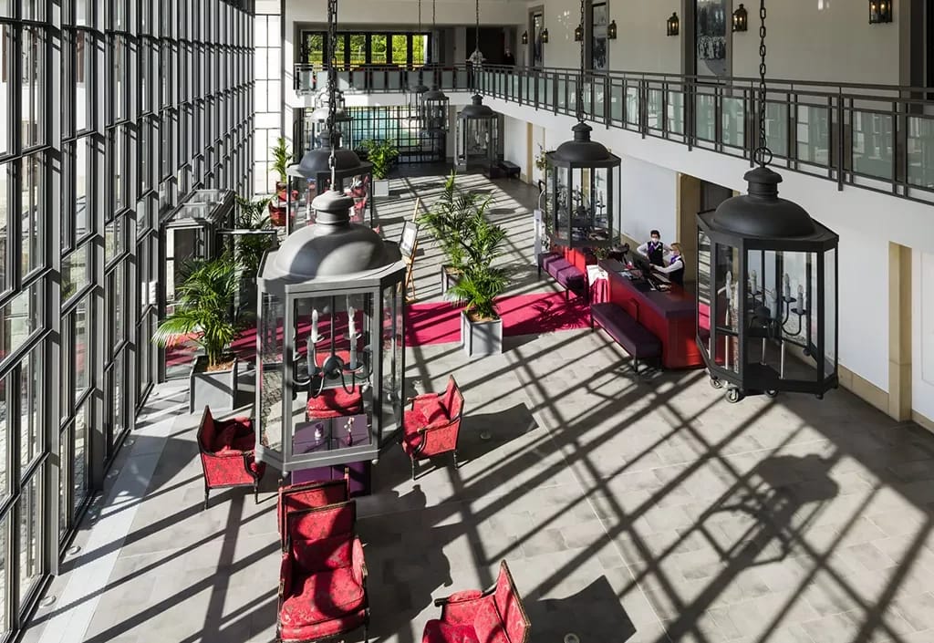 Lichtdurchflutete Lobby mit großen Laternen, roten Sitzmöbeln und hoher Glasfassade