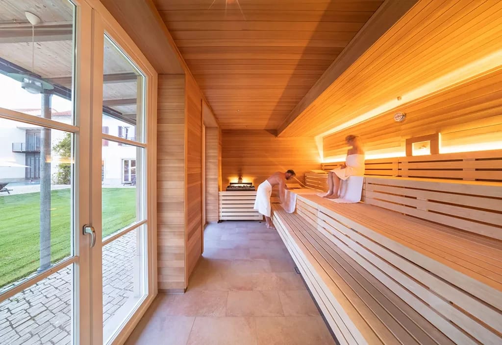 Sauna mit hellen Holzbänken und bodentiefem Fenster mit Blick in den Garten