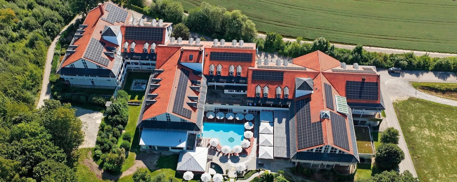 Luftaufnahme der Hotelanlage mit roten Ziegeldächern, Innenhof-Pool und umliegenden Wiesen