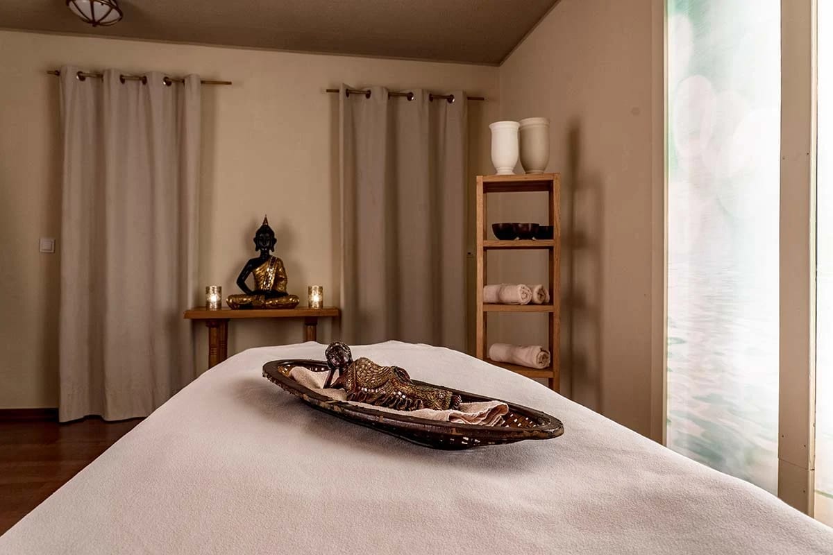 Behandlungsraum mit Massageliege, Dekoschale und Regal mit gerollten Handtüchern