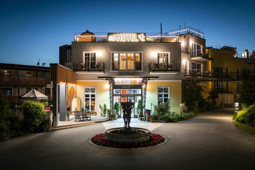 Beleuchtete Hausansicht mit Eingangsbereich, Springbrunnen im Blumenbeet und Dachterrasse in der Abenddämmerung