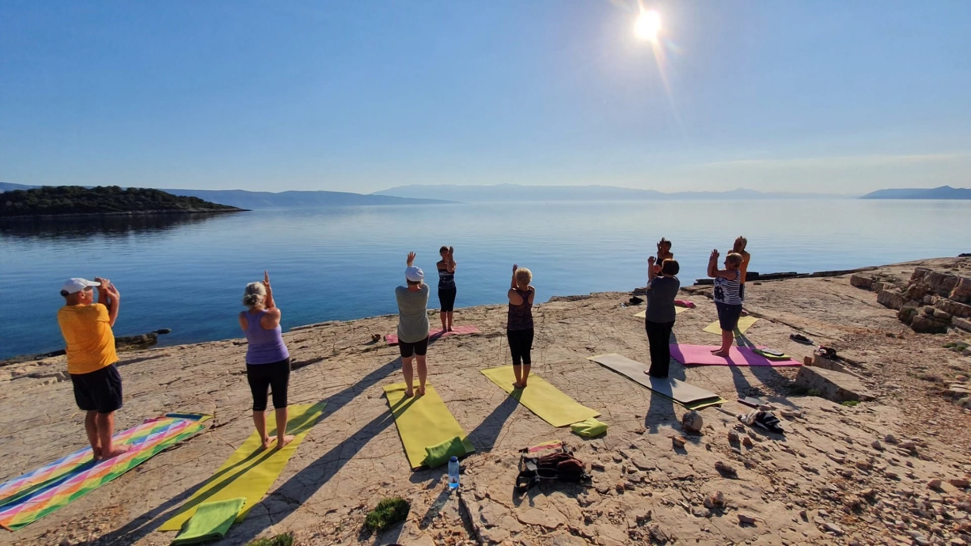 Yogagruppe bei Sonnenaufgang auf Felsen am Meer
