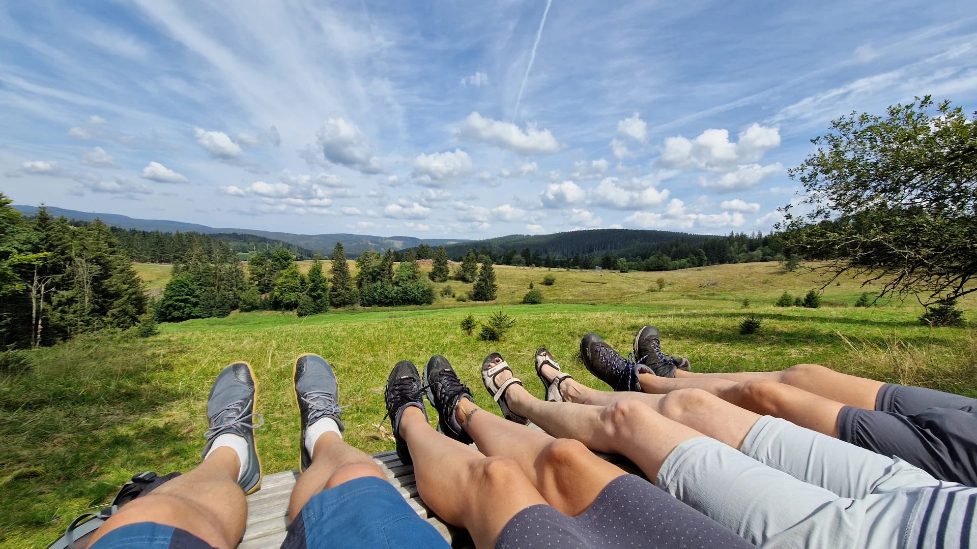Blick über die Landschaft, im Vordergrund die Füße einer rastenden Wandergruppe