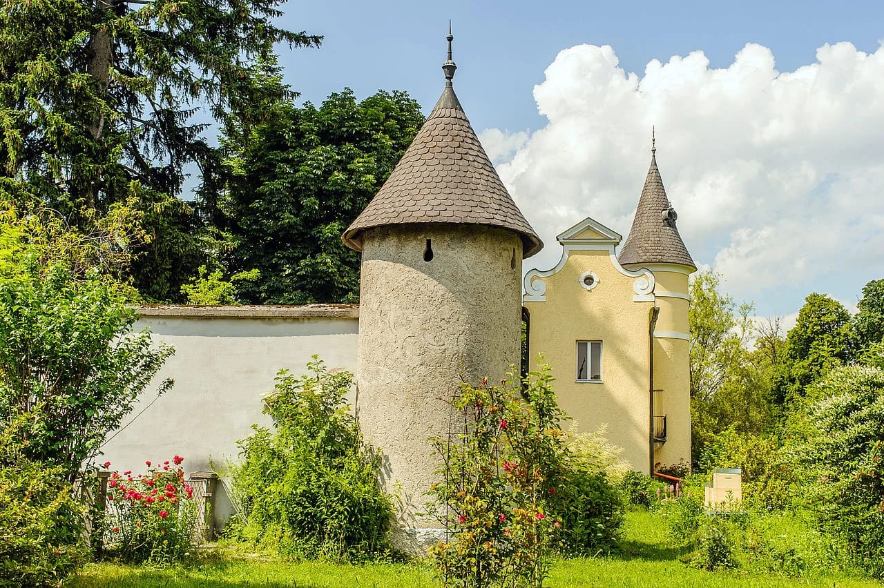 Runder Turm mit Spitzdach im Garten, daneben die gelbe Fassade des Hauses