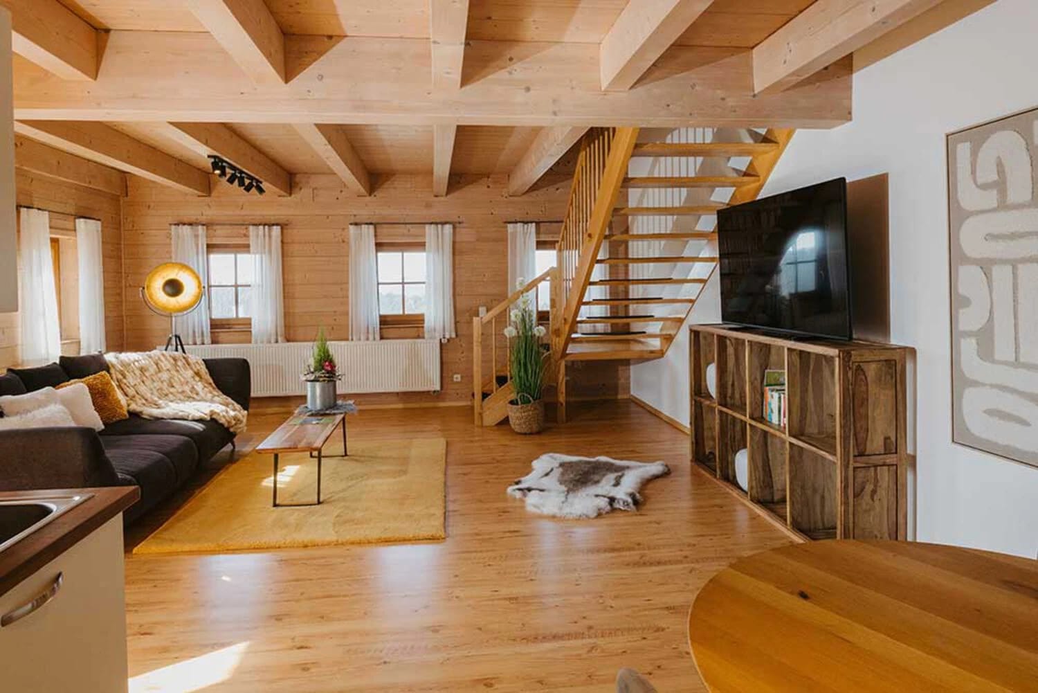 Wohnbereich im Holzhaus mit Holzdecke, Sofa, offener Holztreppe und Fernsehwand
