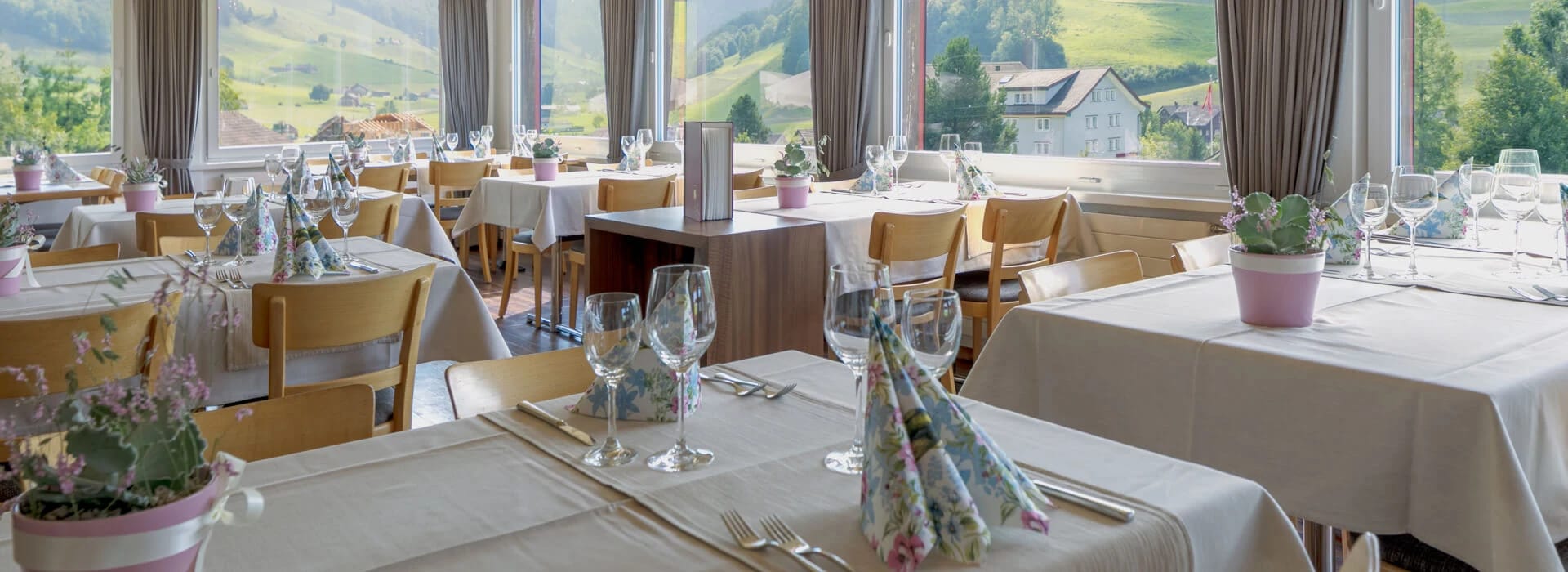 Heller Speisesaal mit gedeckten Tischen und Bergblick durch die Fenster