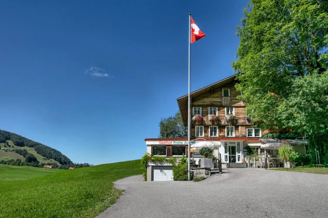 Außenansicht des Hauses mit Schweizer Flagge und grüner Wiese im Sommer