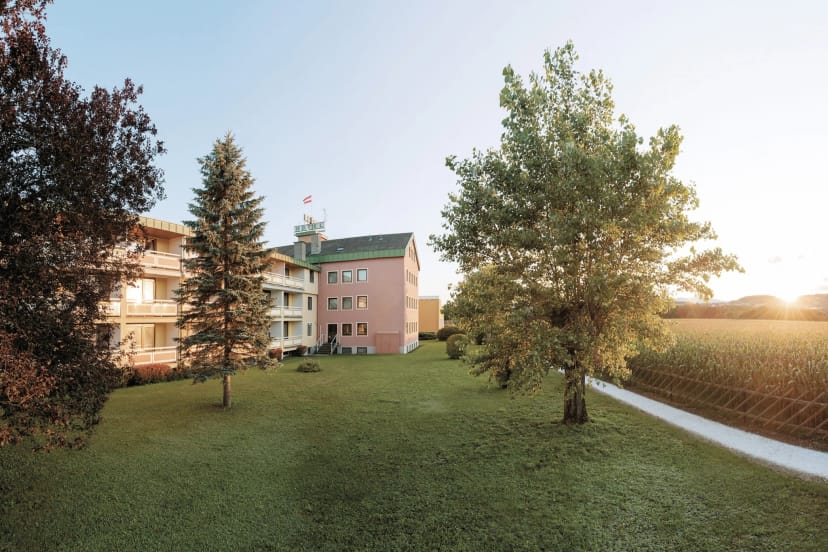 Außenansicht des Wilfinger Ring Bio Hotels mit weitläufigem Garten und Bäumen im Abendlicht