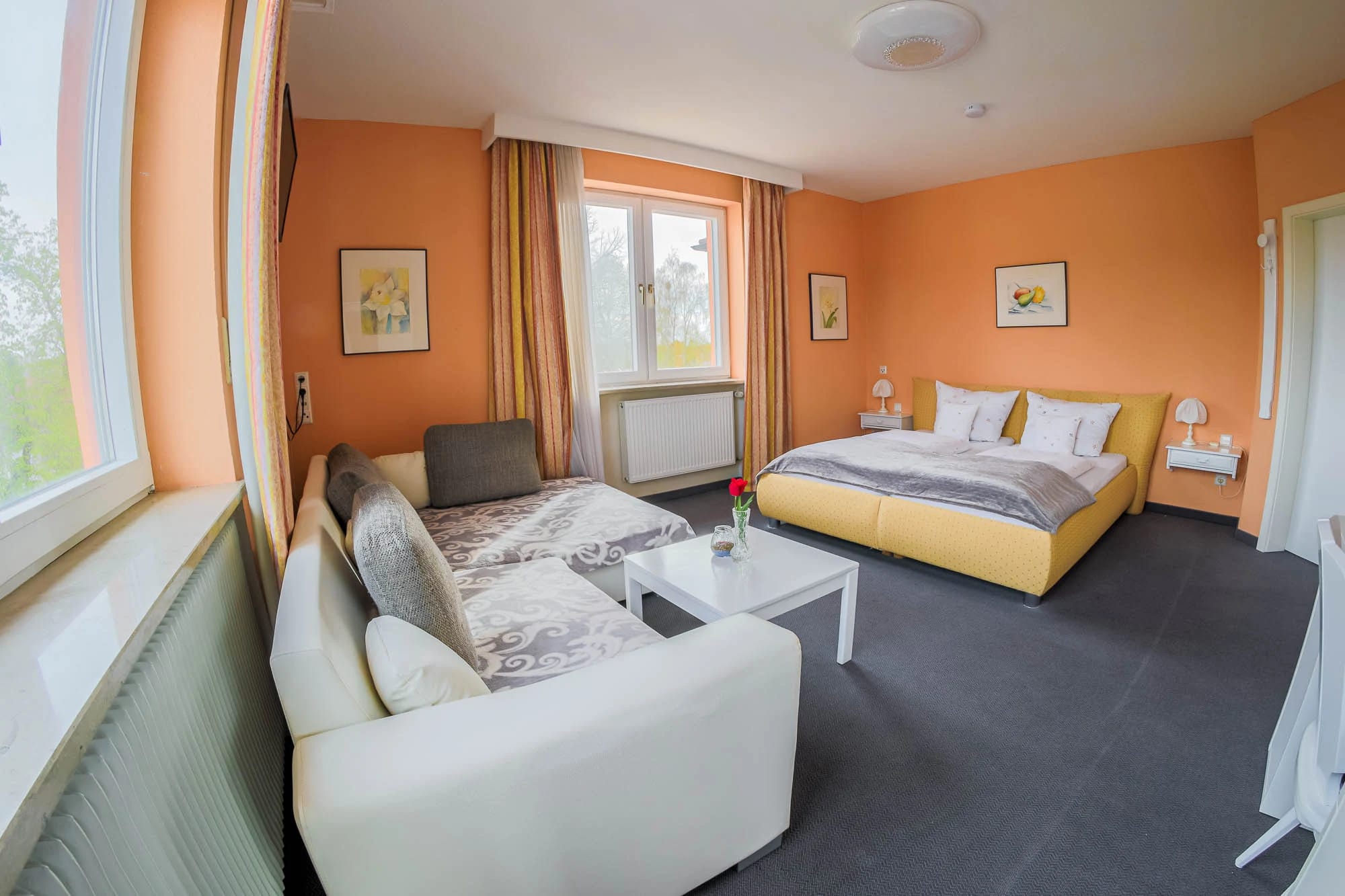 Zimmer mit orangefarbenen Wänden, weißem Sofa, Couchtisch und Doppelbett am Fenster