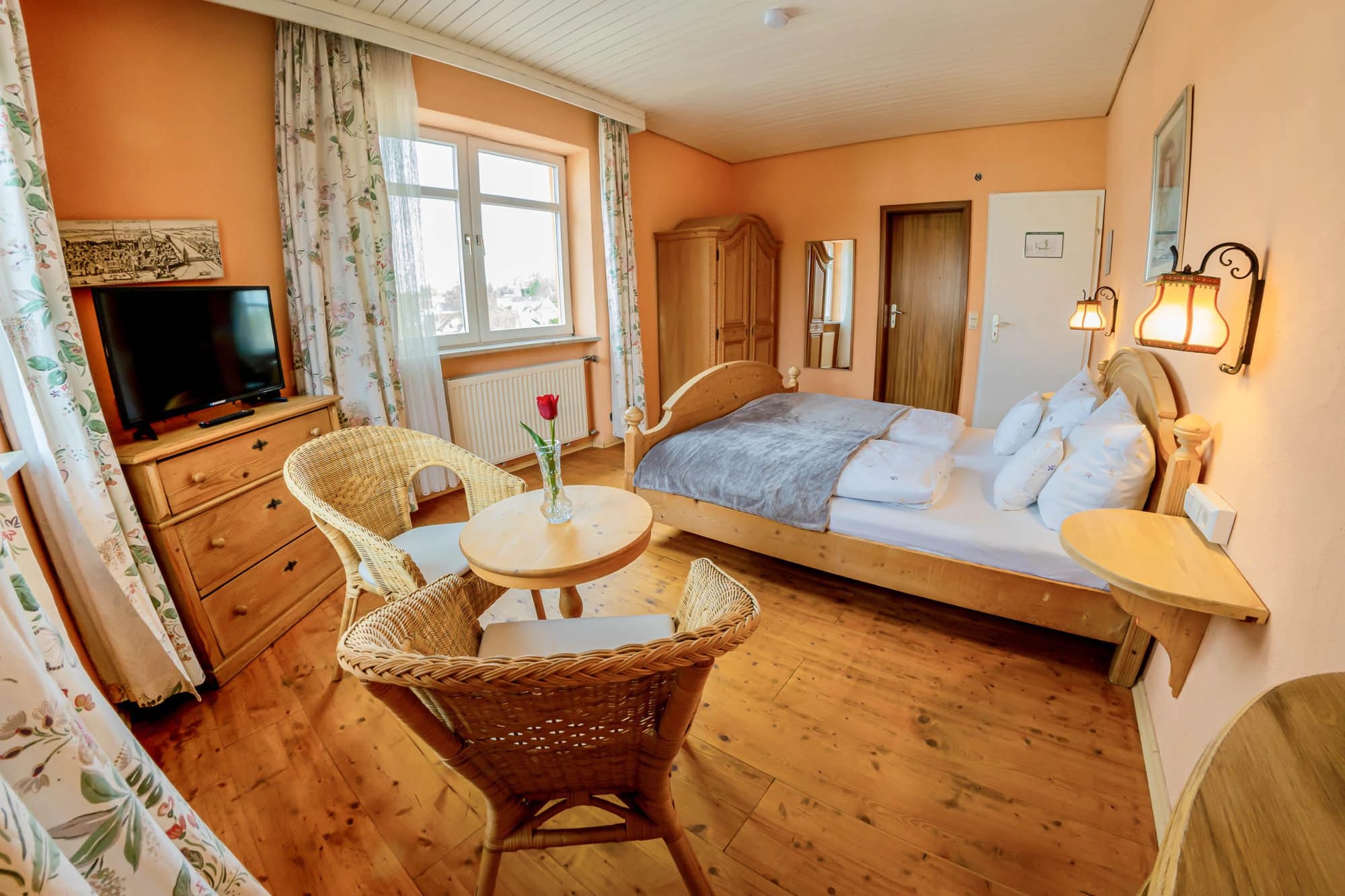 Zimmer im Landhausstil mit Holzmöbeln, Korbstühlen am runden Tisch, Doppelbett und Holzdielen
