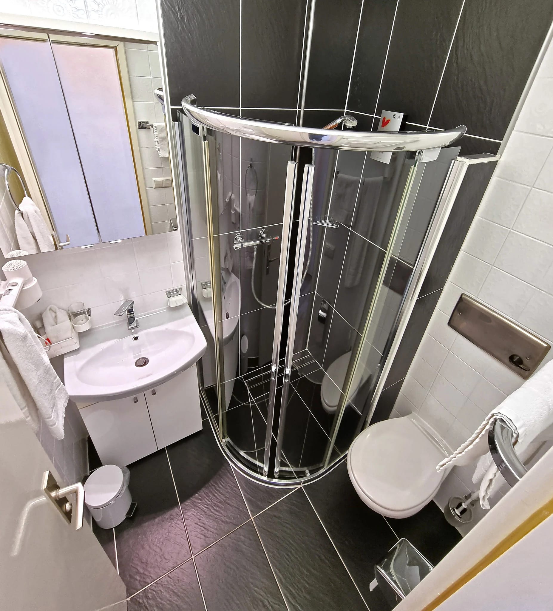 Badezimmer mit runder Duschkabine aus Glas, Waschtisch und dunklen Fliesen