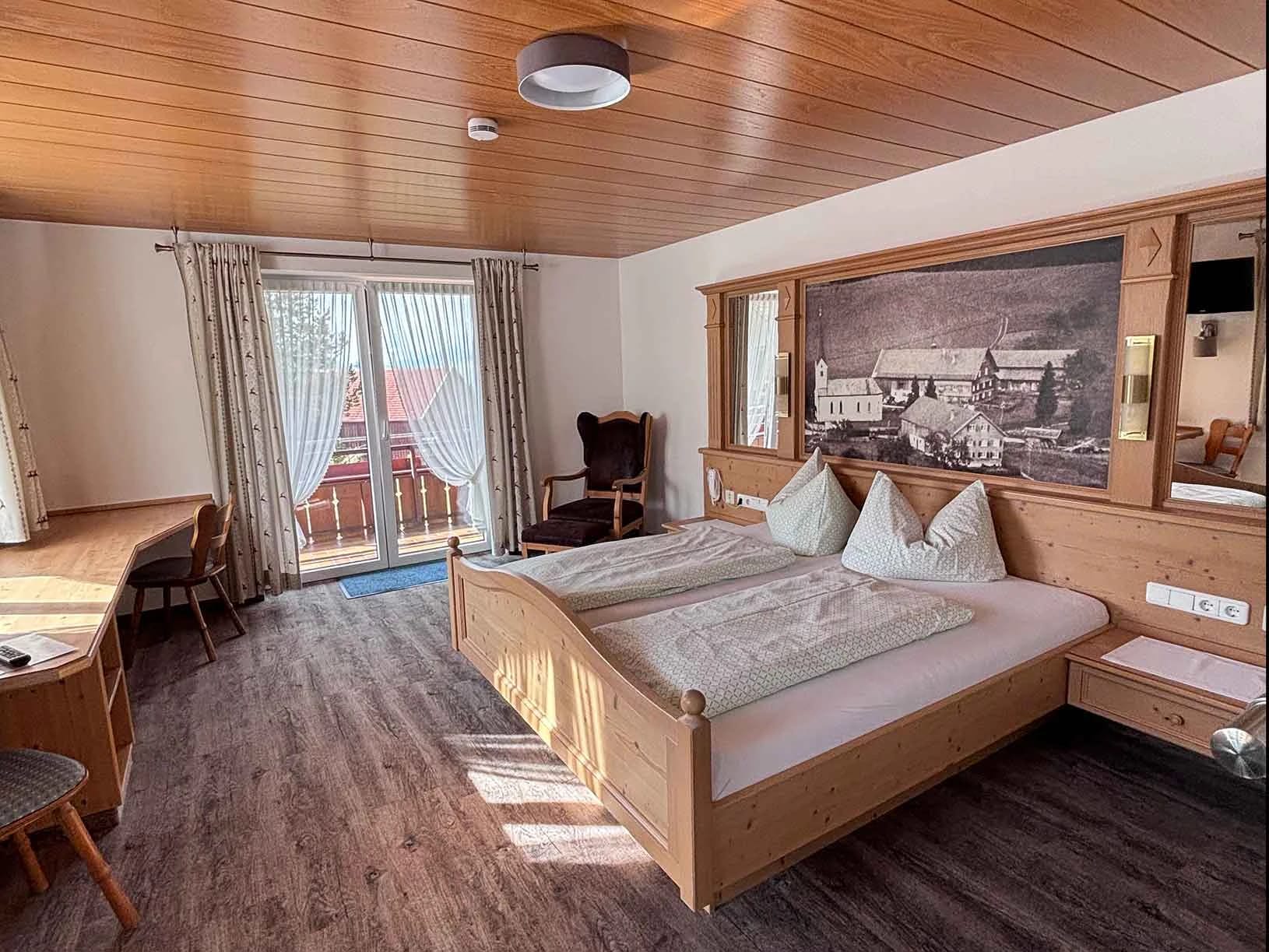 Geräumiges Zimmer mit Doppelbett aus Holz, Schreibtisch und Balkontür