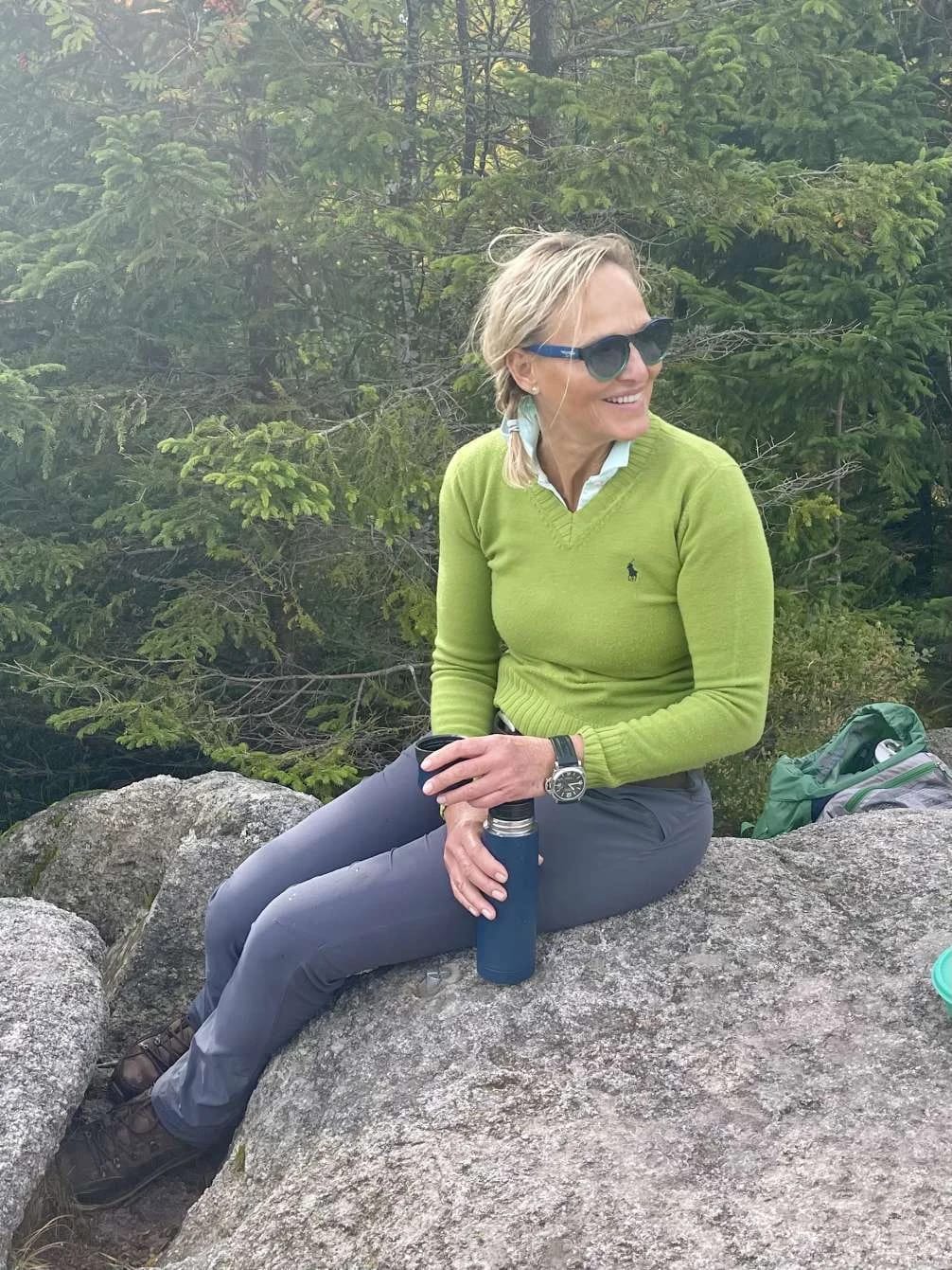 Ute Hesse sitzt auf einem Felsen in den Bergen, eine Trinkflasche in der Hand