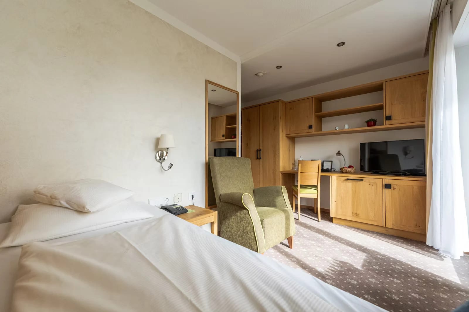 Einzelzimmer mit Bett, Sessel und Schreibbereich